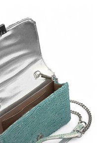 Bolso de mano texturizado en color turquesa con un interior plateado, que presenta una correa de cadena metálica y un cierre a presión, mostrando compartimentos de bolsillo en el interior.