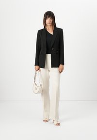 Blazer nero su misura con bottone dorato, abbinato a un top nero, pantaloni a palazzo crema e sandali con tacco beige. Accentuato con una borsa leggera.