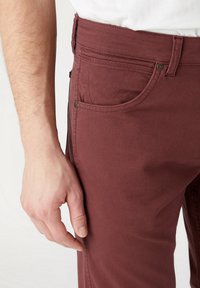 Pantalones vaqueros burdeos con un acabado texturizado, que cuentan con un bolsillo frontal, herrajes de metal y una silueta ajustada.