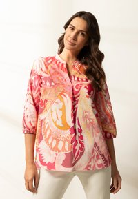 Lekka, wielokolorowa bluzka z kwiatowym wzorem w odcieniach różu, pomarańczu i bieli, z rękawami o długości trzech czwartej oraz stójką.