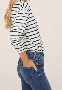 Top de rayas de manga larga en blanco y azul marino, combinado con jeans de mezclilla azules. La parte superior tiene un corte relajado y mangas dobladas.