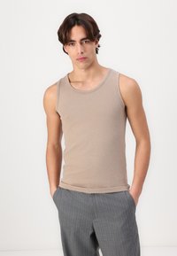 Beige Baumwoll-Top mit Rundhalsausschnitt und geradem Saum, kombiniert mit grauen Nadelstreifen-Hosen. Glatte Textur, lässige Passform.
