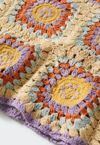 Manta de ganchillo con motivos hexagonales en hilo amarillo, naranja, lavanda y azul claro, con detalles texturizados y bordes en forma de concha.