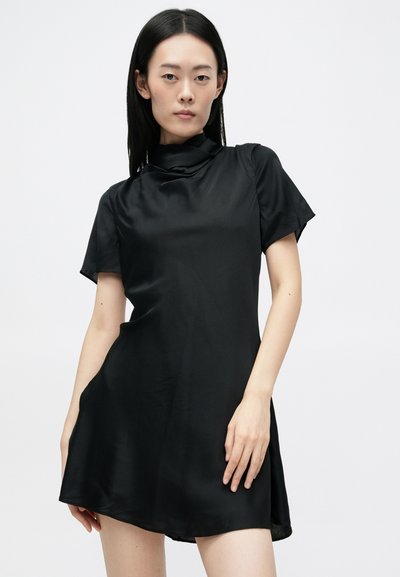 Must püksi kraega must kleit, mis on valmistatud siledast kangast. Kleit on lühikeste varrukatega ja kõige kohal on pingutus, millel on vabalt langev siluett. Sel on lõpetamata äär, mis tagab mugava istuvuse.