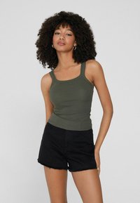 Olivgrünes, geripptes Tanktop mit breiten Trägern, kombiniert mit schwarzen Denim-Shorts mit ausgefransten Kanten und einem lässigen, abgetragenen Look.