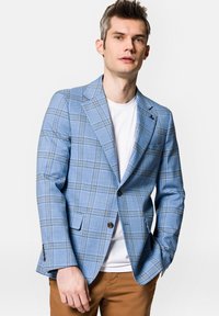 Jasnoniebieski blazer w kratę z dwoma guzikami, klapami i kieszenią na piersi; noszony na białej koszulce z brązowymi spodniami. Gładka struktura materiału.