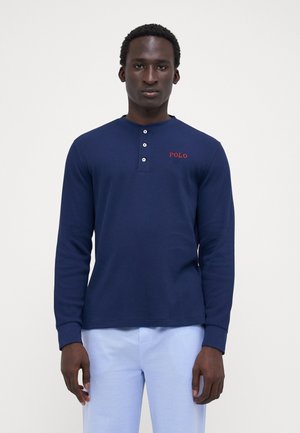 Cămașă henley cu mânecă lungă, de culoare bleumarin, cu un material texturat, guler cu trei butoane și broderie roșie "POLO" pe piept.