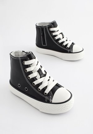 Crne kožne tenisice s visokim gornjim dijelom, bijelim šavovima, gumenim vrhom i bijelim vezicama; imaju bočni patentni zatvarač i otvorene rupice za vezice.