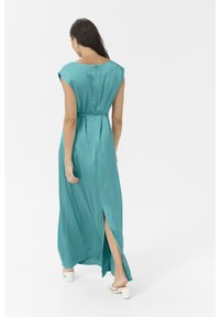 Robe maxi en bleu sarcelle avec des manches courtes, une taille marquée et une fente sur le côté, fabriquée dans un tissu brillant et lisse. L'arrière présente une fermeture en trou de serrure.
