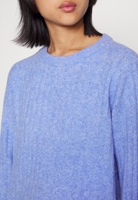 Ljusblå ribbad tröja med rund halsringning, mjuk textur och långa ärmar. Stickmönstret är subtilt och förbättrar tygets utseende.