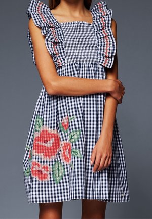 Marineblau-weiß kariertes Kleid mit Rüschenärmeln, gerafftem Oberteil und großer roter und grüner Blumenstickerei auf der Vorderseite.