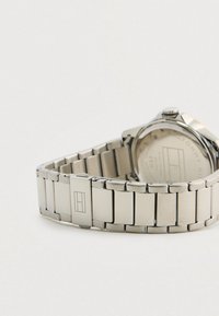 Silver stainless steel bracelet watch with a round case and textured surface, features a logo on the clasp and an engraved back.