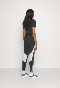 Zwarte sporttop gecombineerd met zwart-grijs gekleurde blokleggings met witte accenten en driedelige streepdetaillering aan de zijkanten.
