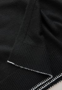 Tissu tricot noir avec une texture côtelée et des bords pliés, présentant un détail de bordure blanche cousue le long de l'ourlet.