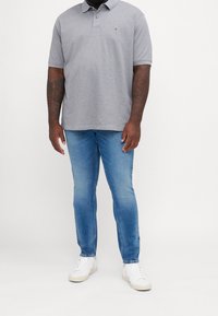 Grå polo skjorta i bomullstyg, slim fit, med krage och två knappar. Kombinerad med ljusblå denimjeans och vita sneakers.