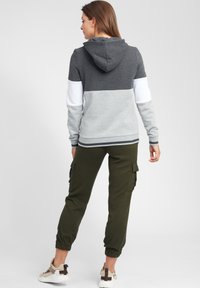 Felpa con cappuccio a blocchi di colore in grigio scuro, grigio chiaro e bianco; abbinata a pantaloni cargo verde oliva e scarpe da ginnastica chiare.