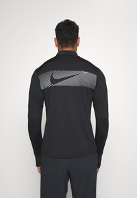 Schwarzes Langarmoberteil mit hohem Kragen, das ein horizontales, weiß gestreiftes Design auf dem Rücken und das Nike-Logo aufweist, aus leichtem Material gefertigt.
