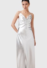 Abito in satin argento con scollatura profonda, dettaglio con coulisse regolabile nella parte anteriore e spalline sottili. Tessuto morbido e lunghezza a terra.