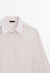 Chemise à manches longues rose clair avec col blanc et poche poitrine sur fond blanc.