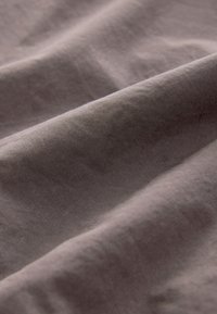 Wrinkled fabric in a muted gray color, featuring a smooth texture with a subtle sheen and soft, flowing drape. No patterns or visible hardware.