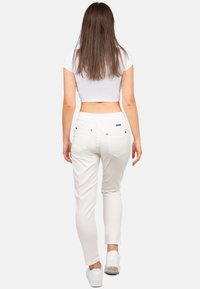 Pantalons blancs ajustés avec taille élastique, deux poches arrière et détails de couture subtils, associés à un crop top blanc et des baskets blanches.