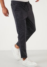 Men's dark grey joggers with a textured fabric and elastic waistband, featuring side pockets and a tapered leg design, paired with white sneakers.