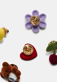 Värikrika broscher med en lila filtblomma, en gul boll, ett rött hjärta, en brun nallebjörn och gröna körsbär med guldhardware.
