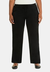 Pantaloni neri, larghi, con vita regolabile con cordino, texture morbida e gambe dritte. Indossati con scarpe nere basse.