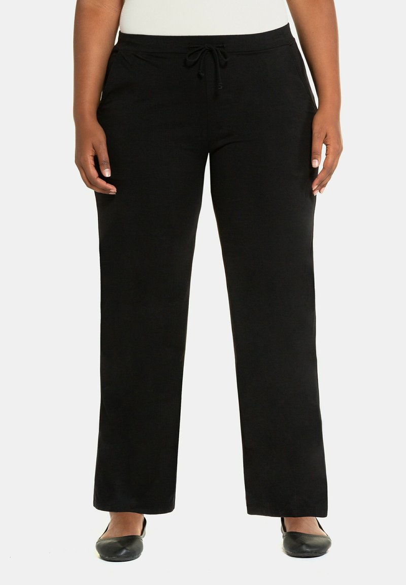Pantaloni neri, larghi, con vita regolabile con cordino, texture morbida e gambe dritte. Indossati con scarpe nere basse.