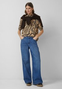 Beež ja must ripp-kraega zebra mustriga kudum, millel on lühikesed varrukad, koos laiade siniste denimihaljadega ning tumeda pruuniga kudumiga, mis on kaela ümber visatud.