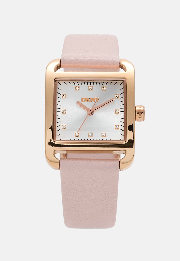 Kwadratowy zegarek DKNY z różowo-złotą metalową kopertą, jasnoróżowym skórzanym paskiem oraz srebrną tarczą z kryształowymi wskaźnikami godzinowymi.