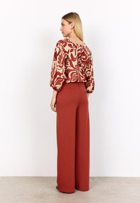Red and beige floral patterned blouse with puff sleeves, paired with high-waisted terracotta wide-leg trousers. Smooth texture, relaxed fit.