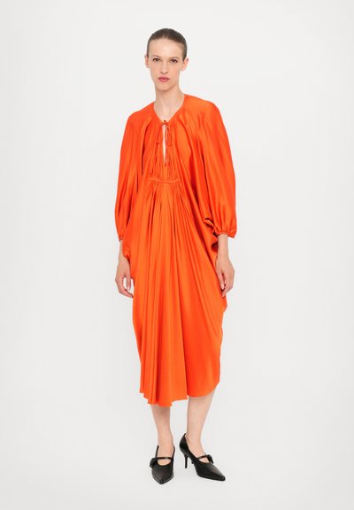 Vestido naranja con mangas largas abullonadas y cintura fruncida. La tela parece lisa; presenta un detalle de abertura y lazo en el escote.