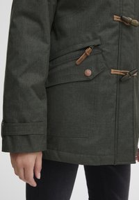 Dark green, textured jacket with a side pocket, brown toggle closures, and a bronze logo button. Crafted from durable fabric.