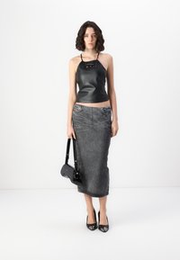 Svart lær crop top med utskjæringsdetaljer, sammen med et langt grått denimskjørt med vertikale striper. Modellen holder en liten svart veske.