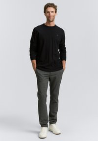 Zwarte langemouwen shirt gecombineerd met grijze broek en witte sneakers. Het shirt heeft een ronde halslijn en getailleerde manchetten, met een subtiel logo.