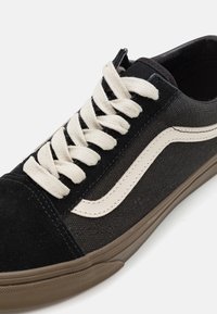 Sort sneakers med ruskind og kanvasmaterialer, cremede snørebånd og en fremtrædende hvid side-stribe. Har en brun gummisål og tekstureret overflade.