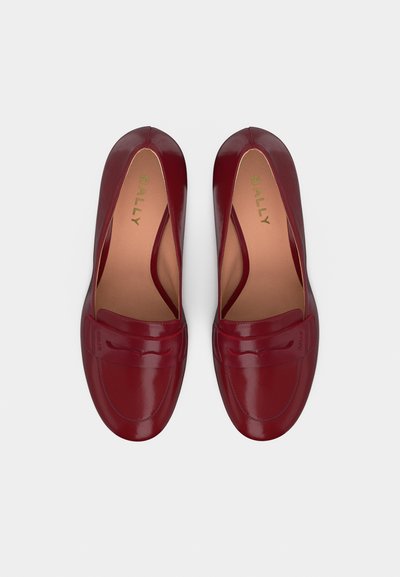 Paire de mocassins en cuir lisse rouge foncé avec un bout arrondi et un détail de bride penny, vue de dessus sur un fond blanc.