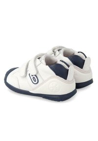 Zapatos infantiles en blanco y azul marino con punta redondeada, tiras de velcro, material de cuero, suela texturizada y un detalle sutil del logo en el lado.