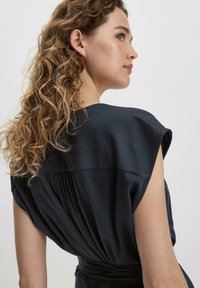 Musta, lyhythihainen mekko, jossa on rento istuvuus, takana gathered-yksityiskohta ja sileä pinta, joka korostaa puhtaita linjoja ja minimaalista muotoilua.