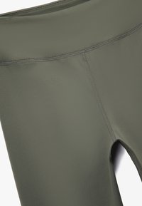 Högmidjade leggings i olivgrönt, gjorda av ett mjukt och elastiskt tyg. Har platta sömmar och en liten utskärning vid ankeln.