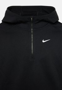 Haut à zip demi-longue noir de Nike en tissu texturé, avec une capuche, une fermeture éclair argentée et un logo blanc sur la poitrine gauche.