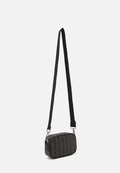Sac bandoulière noir avec un motif géométrique texturé, des accents lisses et une longue sangle réglable avec quincaillerie métallique.
