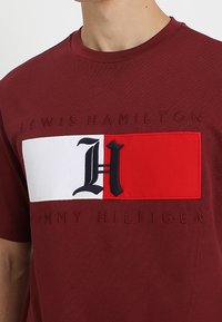 Burgundy cotton t-shirt featuring a block graphic with a white and red design. Embroidered text 'Lewis Hamilton' and 'Tommy Hilfiger' at the bottom.
