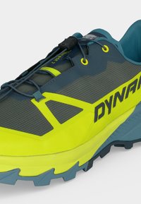 Ανδρικό παπούτσι για τρέξιμο σε μονοπάτια σε κίτρινο και γκρι με πλέγμα στο επάνω μέρος, σύστημα δέσιμου με κούμπωμα και υφή μπλε σόλας.