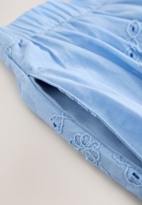 Blusa di cotone azzurro chiaro con motivi floreali ricamati lungo l'orlo e la spalla, con dettaglio arricciato al collo.