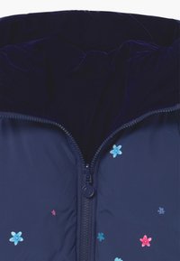Námořnická prošívaná bunda se zipem, sametově podšitá kapuce a květinovou výšivkou v modré a růžové na přední straně.