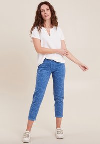 Weißes kurzärmeliges Oberteil mit V-Ausschnitt, kombiniert mit blauen gemusterten Hosen mit Paisleymuster und hochgerollten Säumen. Tragen mit weißen Sneakers.