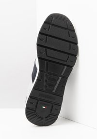 Suola in gomma nera con modelli di grip texture, caratterizzata da una parte superiore bianca e blu, etichettata con "NeroGiardini" e un accento della bandiera italiana.