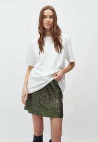 T-shirt bianco in cotone a maniche corte abbinato a una mini gonna verde con paillettes. La gonna ha una texture lucida e un orlo a punta.
